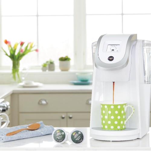 white keurig coffee maker with green polka dot mug and two kcups pods on counter in farmhouse kitchen setting