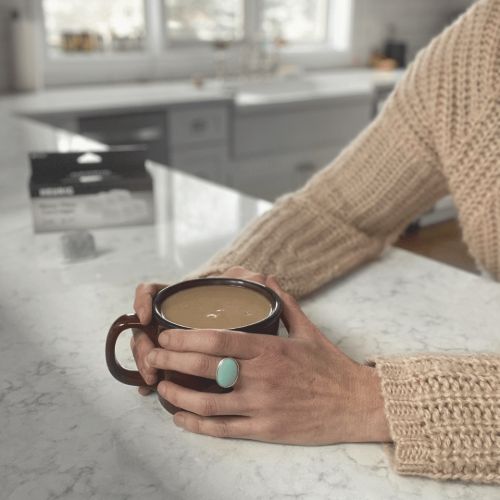 hands on kitchen counter holding a dark brown coffee mug